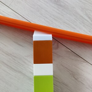 May include: A stack of three colorful blocks, orange, white, and green, with a bright orange track piece resting on top of the orange block.