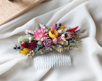 May include: A white comb with dried flowers in shades of pink, yellow, red, and purple. The flowers are arranged in a cluster on the comb.