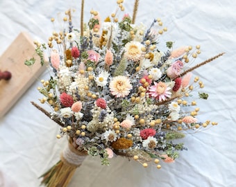 May include: A dried flower bouquet with a variety of colors, including pink, white, and yellow. The bouquet is tied with a natural twine and has a light pink ribbon.