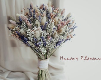 May include: A bouquet of dried flowers in shades of purple, pink, and white. The bouquet includes lavender, bunny tails, and other dried grasses. The bouquet is tied with a white ribbon and the text "Heaven Flowers" is visible in the bottom right corner of the image.