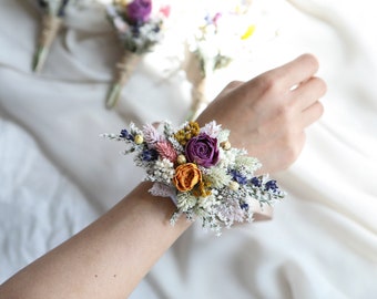 May include: A wrist corsage made with dried flowers. The corsage features a mix of purple, orange, and white flowers.