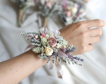 May include: A wrist corsage made with dried flowers in shades of pink, white, and lavender. The corsage is tied with a white satin ribbon.