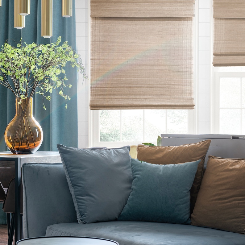 K&ouml;nnte beinhalten: Ein Wohnzimmer mit einem Sofa, Kissen und einem Fenster mit Bambusjalousien. Das Sofa ist hellblau und die Kissen sind in Blau- und Braunt&ouml;nen gehalten. Die Jalousien sind hellbraun und heruntergelassen, um das Fenster zu bedecken.