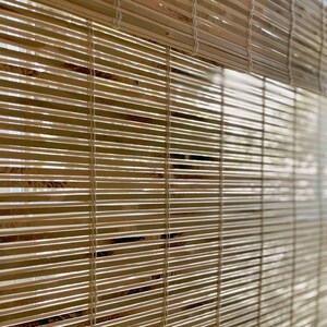 May include: Close-up of a natural woven bamboo window blind in a light brown colour. The blind is made of thin strips of bamboo that are woven together with white string.