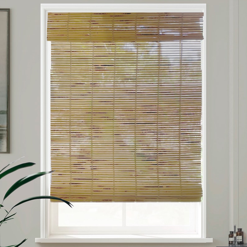 May include: Natural woven bamboo window blinds in a light brown colour. The blinds are raised to reveal the white window frame behind them.
