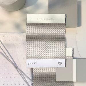 K&ouml;nnte beinhalten: Ein gewebtes Stoffmuster in hellbrauner Farbe mit dem Text "WOVEN COLLECTION" und "sand" darauf gedruckt. Das Muster wird mit einem wei&szlig;en und einem grauen Musterkarten gezeigt.