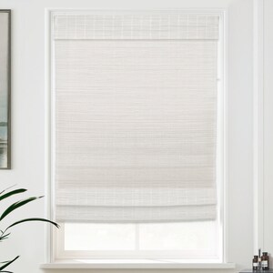 May include: White roman blind with a woven texture. The blind is raised, revealing a window with a white frame.
