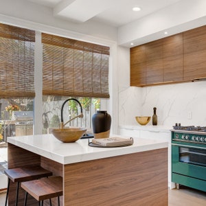 May include: A modern kitchen island with a white worktop and a wooden base. The island has a large sink with a gold tap, a bowl, and a book on top. The kitchen has a green stove and a white worktop with a gold bowl.