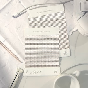 K&ouml;nnte beinhalten: Zwei Stoffmuster aus gewebtem Stoff in hellbeige mit einem dezenten Muster. Die Stoffmuster sind mit "WOVEN COLLECTION" und "Frost White" beschriftet.