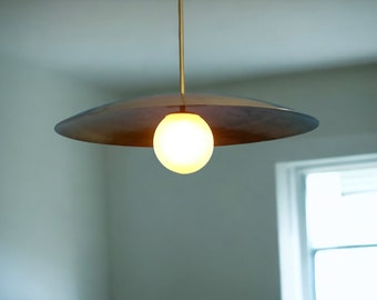 Peut inclure: Un luminaire suspendu moderne et minimaliste avec un abat-jour rond en verre blanc et une canopée circulaire plate en métal. La lumière est suspendue à un seul cordon.
