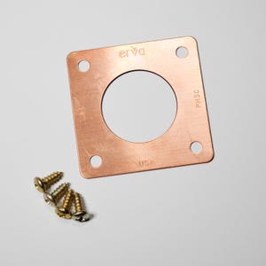 May include: A copper-colored square plate with a central circular opening and four corner holes. The plate has the text "erva" and "USA" printed on it. Several gold-colored screws are positioned near the plate.