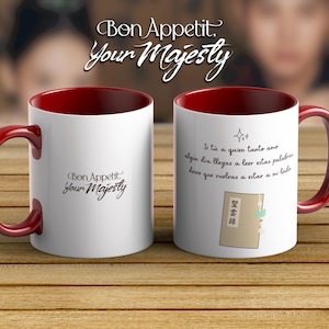 May include: White ceramic mug with a red interior and handle. The mug features the text "Bon Appetit, Your Majesty" in a script font. The other side has a poem in Spanish and a drawing.