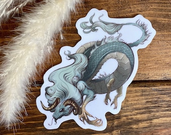 May include: A sticker featuring a detailed illustration of a blue and white dragon with a long, flowing mane. The dragon is curled up in a defensive position, with its claws extended.