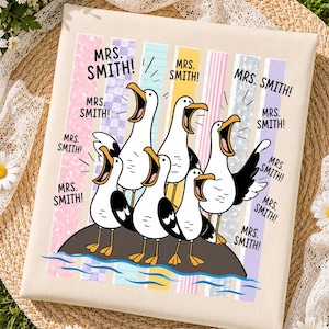 May include: A square canvas print featuring five cartoon seagulls standing on a rock, all with open beaks. The text "MRS. SMITH!" is repeated multiple times around the birds. The background consists of vertical pastel-colored stripes.