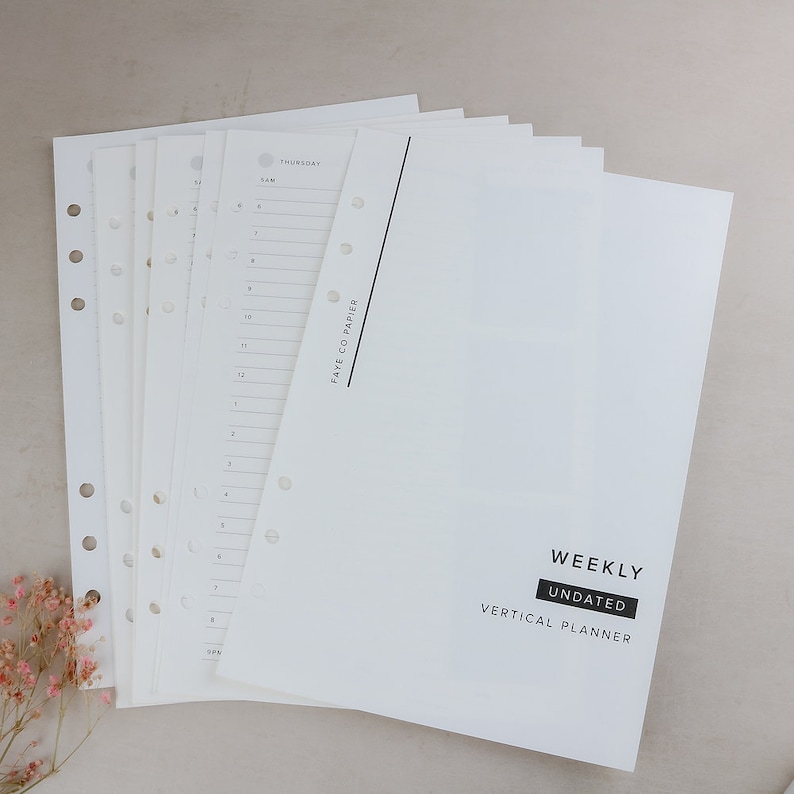 May include: A stack of white undated weekly vertical planner pages. The pages are pre-punched with holes for binding. The cover page has the words "WEEKLY UNDATED VERTICAL PLANNER" in a black rectangle.