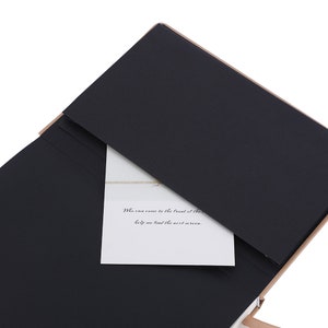 K&ouml;nnte beinhalten: Eine schwarze Pr&auml;sentationsmappe mit hellbraunem Rand und einer wei&szlig;en Karte im Inneren. Auf der Karte steht: "Who can come to the front of the help me find the next screen."