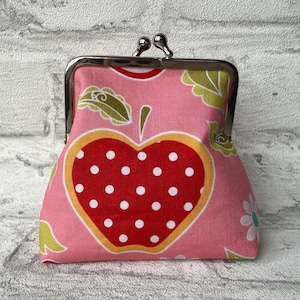May include: A pink fabric coin purse with a red and white polka dot apple design. The purse has a silver metal frame.