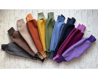 May include: A collection of fleece arm warmers in various colors, including gray, brown, tan, orange, yellow, green, blue, black, burgundy, and purple. Each arm warmer has a contrasting cuff and collar, and they are arranged in a fan shape.