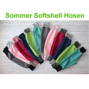 Könnte beinhalten: Eine Auswahl an bunten Softshellhosen mit grauen Bündchen. Die Hosen sind in einem Halbkreis auf einer hellen Holzoberfläche angeordnet. Der Text "Sommer Softshell Hosen" ist oben im Bild zu sehen.