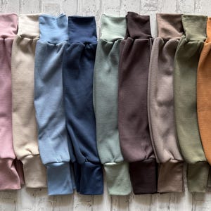 Könnte beinhalten: Eine Kollektion von zehn Hosen aus Rippstrick, die nebeneinander in einem Farbspektrum aus Violett, Hellrosa, Creme, Hellblau, Marineblau, Salbeigrün, Dunkelbraun, Taupe, Olivgrün und Senfgelb angeordnet sind und über gerippte Beinabschlüsse verfügen.