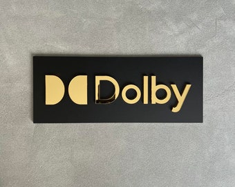 May include: A black rectangular sign with the gold text "Dolby" and two gold stylized "D"s.