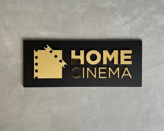 May include: Black rectangular sign with gold lettering that reads "HOME CINEMA". A gold film reel icon is to the left of the text.