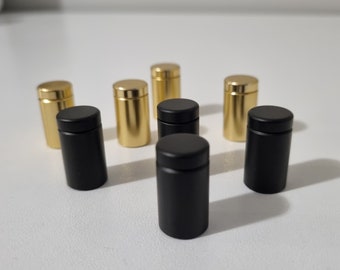 May include: A set of eight cylindrical display stands, four are black and four are gold. The stands are made of metal and have a smooth finish.