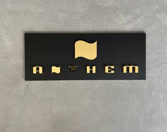 May include: A black sign with gold lettering that reads "ANTHEM" with a gold stylized flag icon above the word.