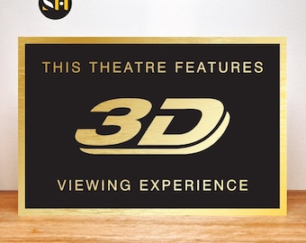 May include: A gold plaque with black background and gold lettering that reads "This theatre features 3D viewing experience".