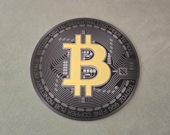 May include: A black and gold Bitcoin coin with the text "FINE COPPER 999 M/B MONETARY METALS BITCOIN DIGITAL DECENTRALIZED - PEER TO PEER 1 TROY OZ"