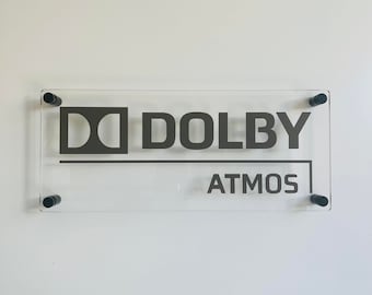 May include: A clear acrylic sign with black screws and the text "Dolby Atmos" in black lettering.