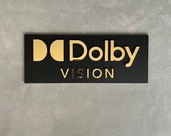 May include: Black rectangular sign with gold lettering that reads "Dolby Vision".