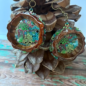 Puede incluir: Pendientes hechos a mano con un diseño único. Presentan un marco circular marrón y un interior texturizado y colorido, con una mezcla de azul, verde, rojo y amarillo. Los pendientes cuelgan de ganchos dorados.