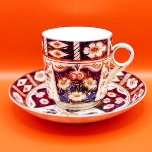 May include: A white porcelain teacup and saucer with a blue and red floral pattern. The cup has a gold rim and a handle. The saucer has a matching pattern.