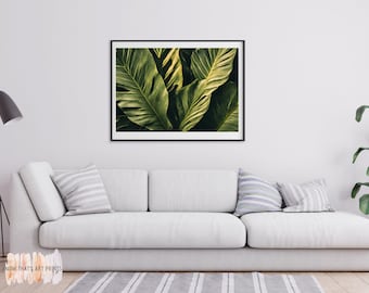 May include: A framed art print featuring a close-up of large, green tropical leaves with prominent veins. The leaves have varying shades of green and yellow, creating a sense of depth and texture. The artwork is displayed above a white sofa.