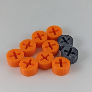 May include: A collection of orange and gray screw head covers. The orange covers have a cross-shaped indentation, while the gray ones have a similar design. The objects are arranged on a white surface.