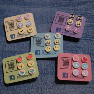 May include: Five sets of colourful polymer clay earrings with various designs, including hearts, strawberries, lightning bolts, skulls, and animal prints. Each set is displayed on a card with the text "Idle Thumbs Studio" and "Find us on Facebook".