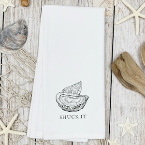 May include: White kitchen towel with a black and white illustration of an oyster with a lemon wedge and the text "SHUCK IT".
