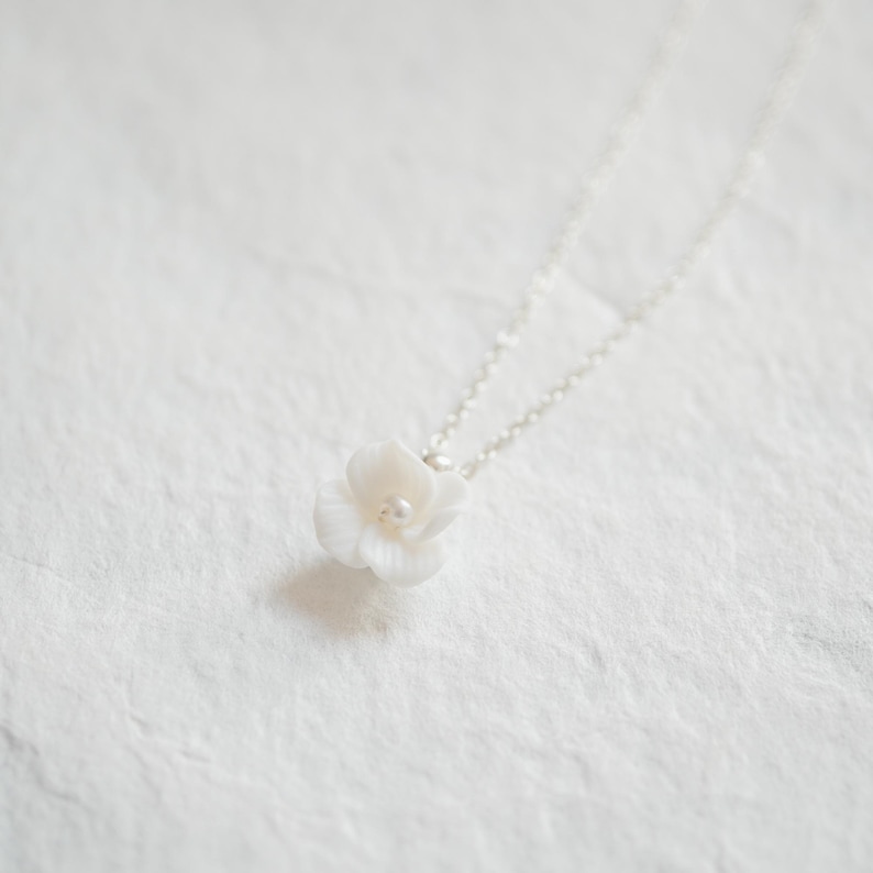 May include: A delicate white flower pendant necklace with a small pearl accent. The necklace is made of silver chain and features a simple, elegant design.