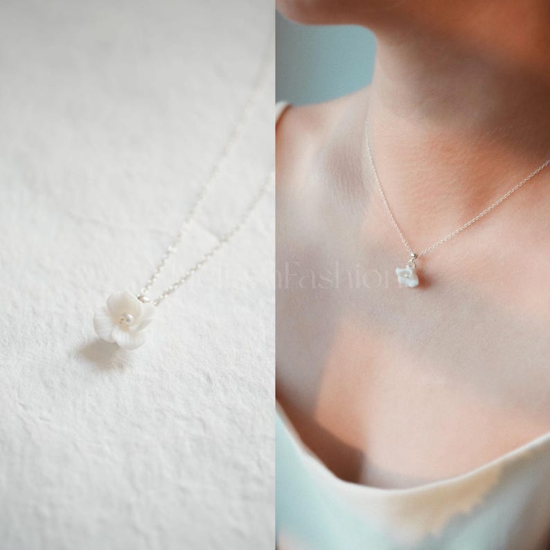 May include: A delicate silver chain necklace with a small white flower pendant. The flower has a pearl in the center.