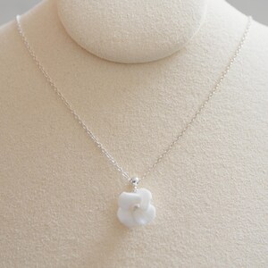 May include: A delicate silver chain necklace with a white porcelain flower pendant.