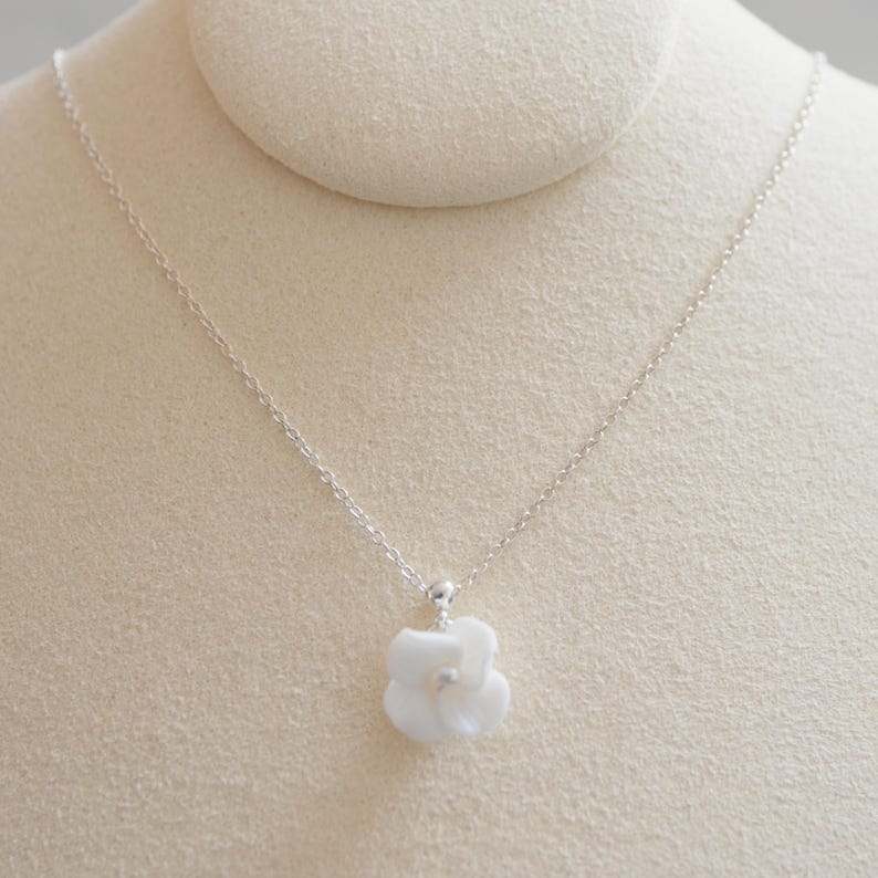 May include: A delicate silver chain necklace with a white porcelain flower pendant.