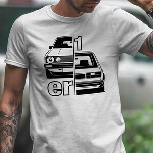 Könnte beinhalten: Weißes T-Shirt mit einer schwarz-weißen Grafik eines geteilten Autos mit dem Text "1 er". Das T-Shirt wird von einer Person im Freien getragen. Die Person trägt eine braune Cargohose.