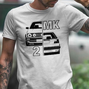 Könnte beinhalten: Ein weißes T-Shirt mit einer schwarzen Grafik von zwei Autos, einem Volkswagen Golf MK2 und einem Volkswagen Golf MK1, mit dem Text "MK2" auf der Vorderseite.