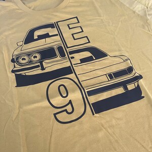 Könnte beinhalten: Ein gelbes T-Shirt mit einem schwarzen Grafikdesign aus zwei Autos und der Zahl 9. Die Autos sind in Schwarz umrandet und haben einen Vintage-Look. Die Zahl 9 ist groß und fett.