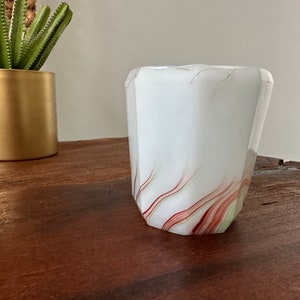 May include: White glass vase with red and green swirl pattern. The vase has a hexagonal shape.