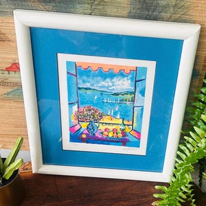 May include: A framed print featuring a colorful painting of a coastal view through an open window. The scene includes a vase of flowers, a bowl of fruit, and a bottle on a table, with sailboats on the water under a bright blue sky and orange awning.