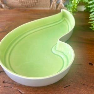 May include: A light green ceramic serving dish shaped like a leaf. The dish has a white rim and a smooth, glossy finish.