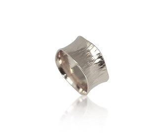 May include: A silver ring with a textured, wide band. The band is slightly curved and has a unique, organic shape.
