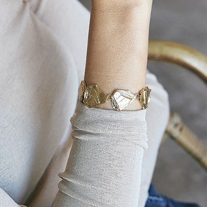 May include: A gold bracelet with a chain made of linked, textured, leaf-shaped pieces.